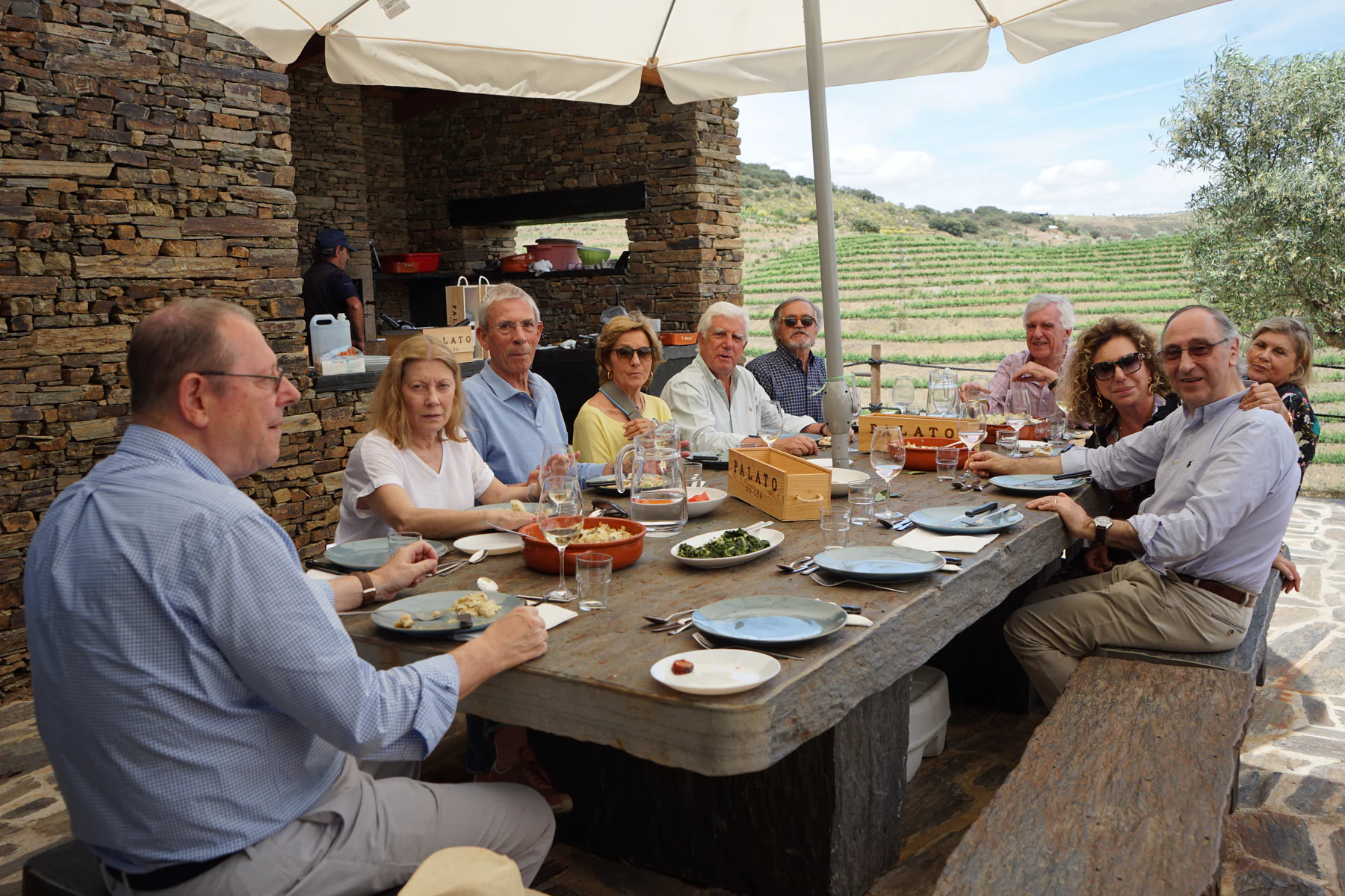 Amigos reunidos à mesa de pedra, diante da vinha